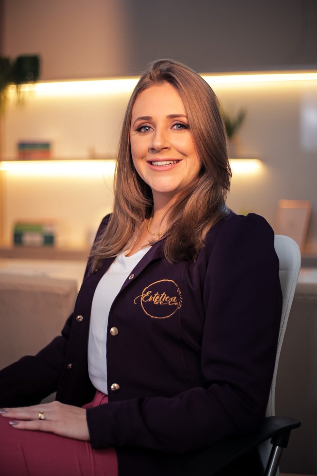 Eduarda Machado com cardigã vinho de logo bordado, sentada no consultório